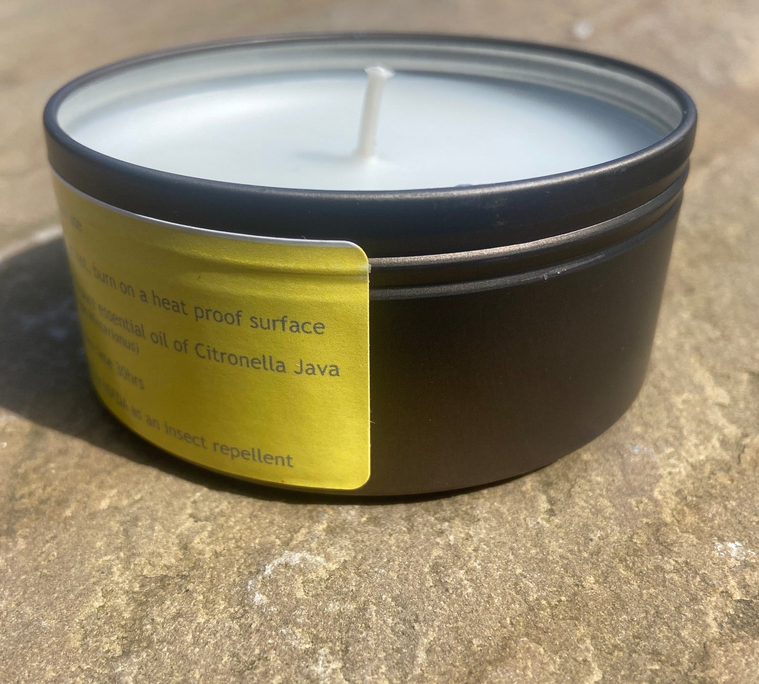 Citronella candle in a bronze tin with a yellow label on a stone  surface