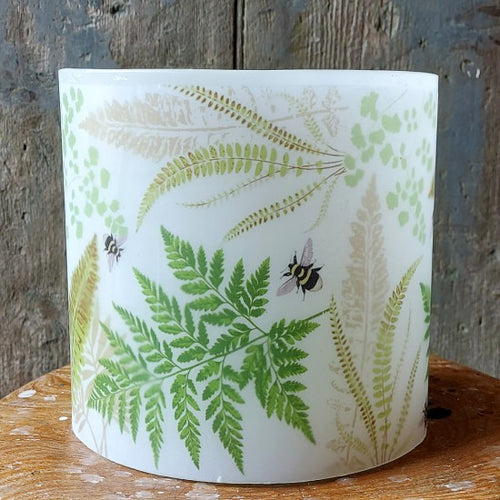 White candle with green leaf and bee design on a wooden surface and rustic background