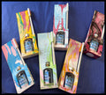 Five bottles of Tahiti Breeze reed diffuser with colorful abstract-patterned boxes arranged on a dark blue fabric background.