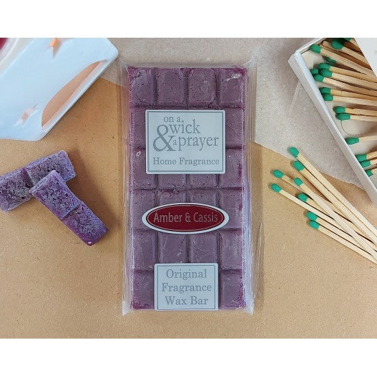 Wax Melt bar with packaging labeled 'On a Wick & Prayer' fragrance Amber and Cassis on a wooden surface with matches.