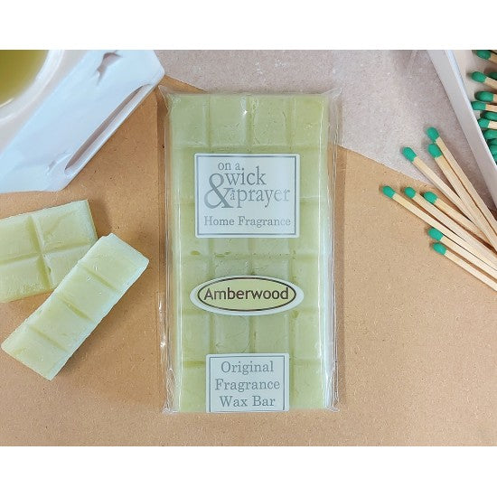 Wax bar in Amberwood scent with 'On a Wick & Prayer' branding on a wooden surface with wax bars and matches.