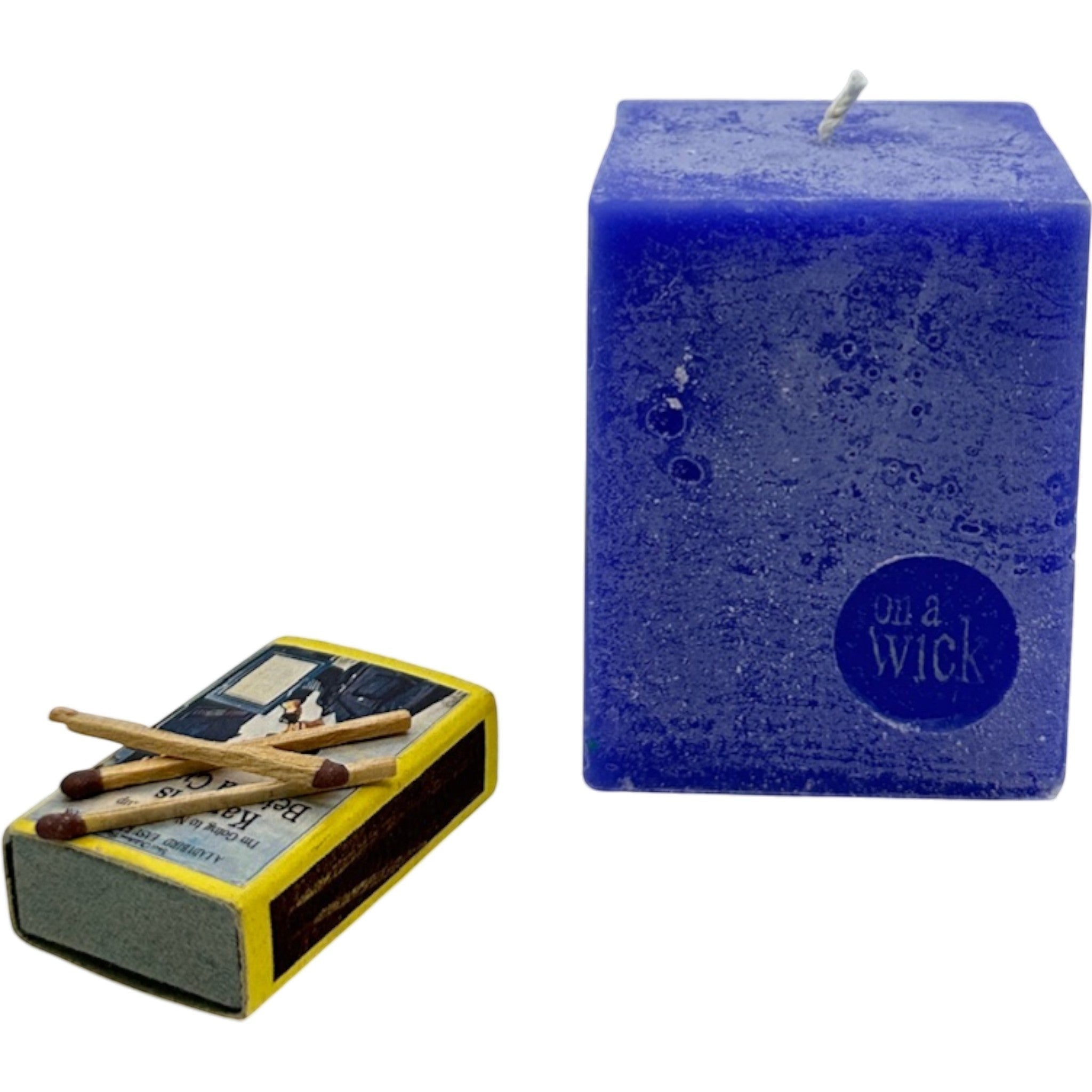 On a Wick and a Prayer blue square pillar candle with a textured finish and a circular embossed logo. Includes a box of matches.