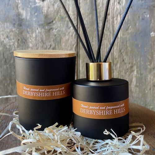 On a Wick and a Prayer black matte candle with bamboo lid and reed diffuser with gold accent, both labelled Derbyshire Hills.