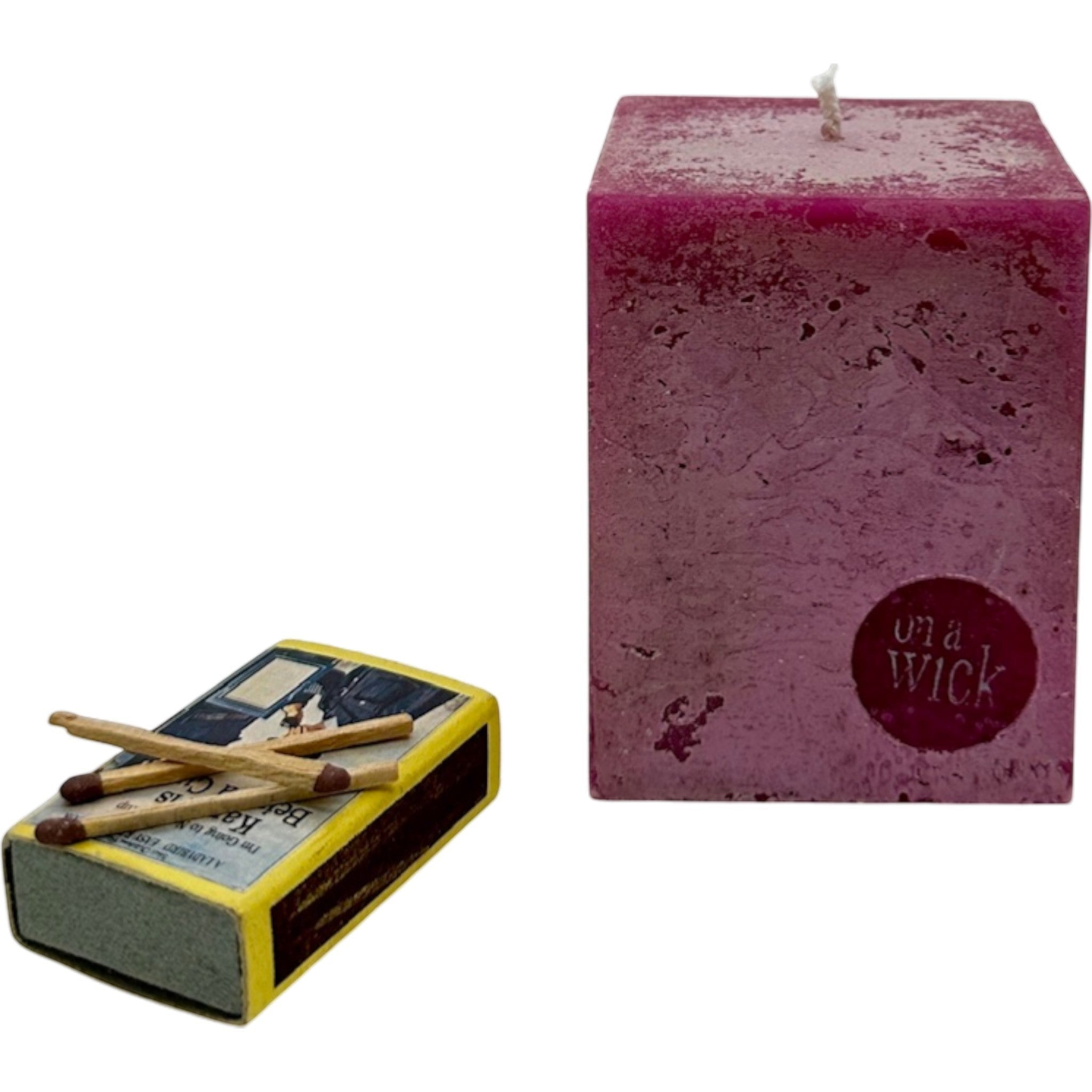 On a Wick and a Prayer magenta square pillar candle with textured finish and a box of matches.