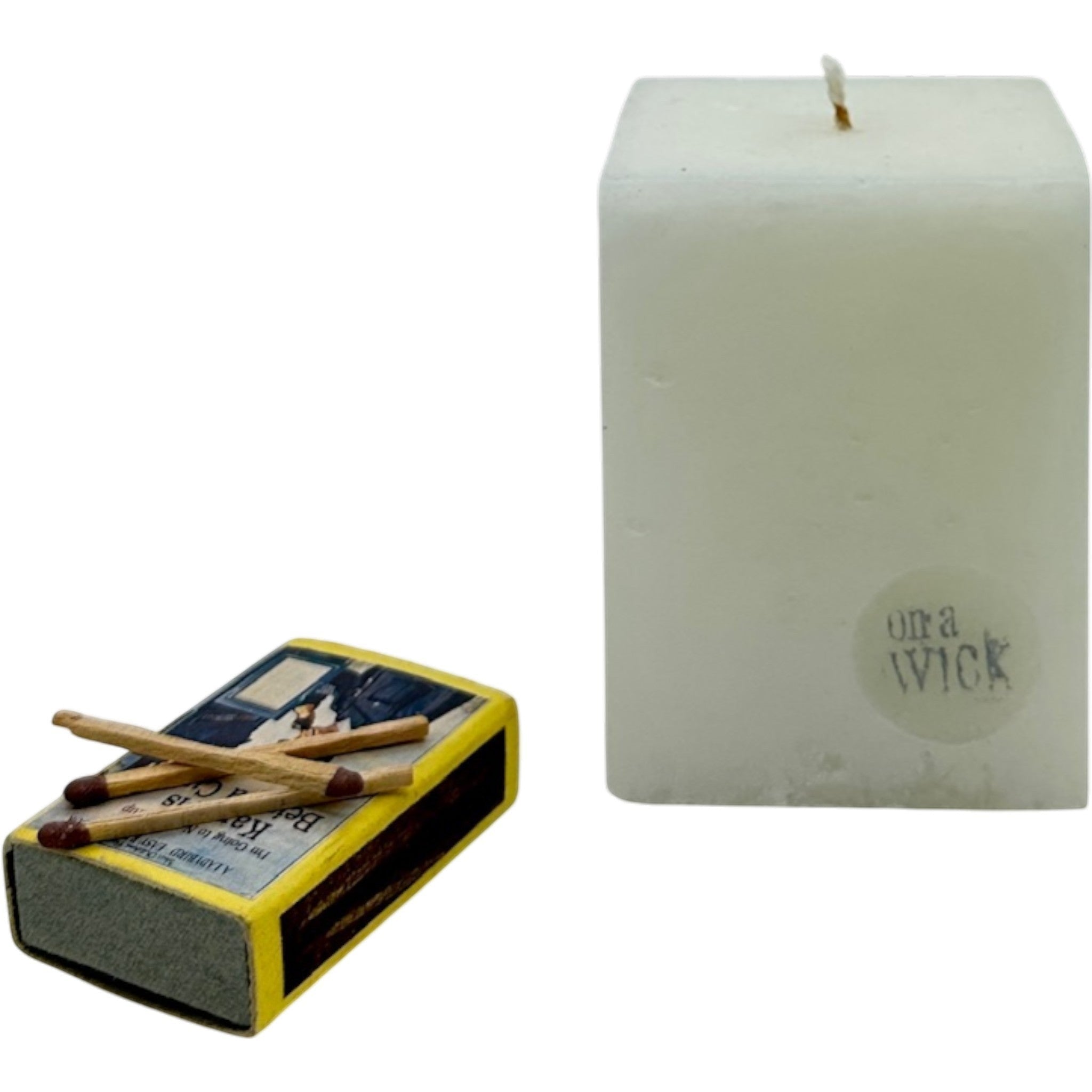 On a Wick and a Prayer white square pillar candle with a wick and a vintage matchbox.